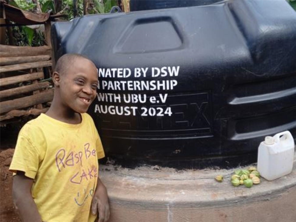 "Jonathan lächelt neben seinem grünen Regenwassertank im Garten, nachhaltige Wassernutzung"