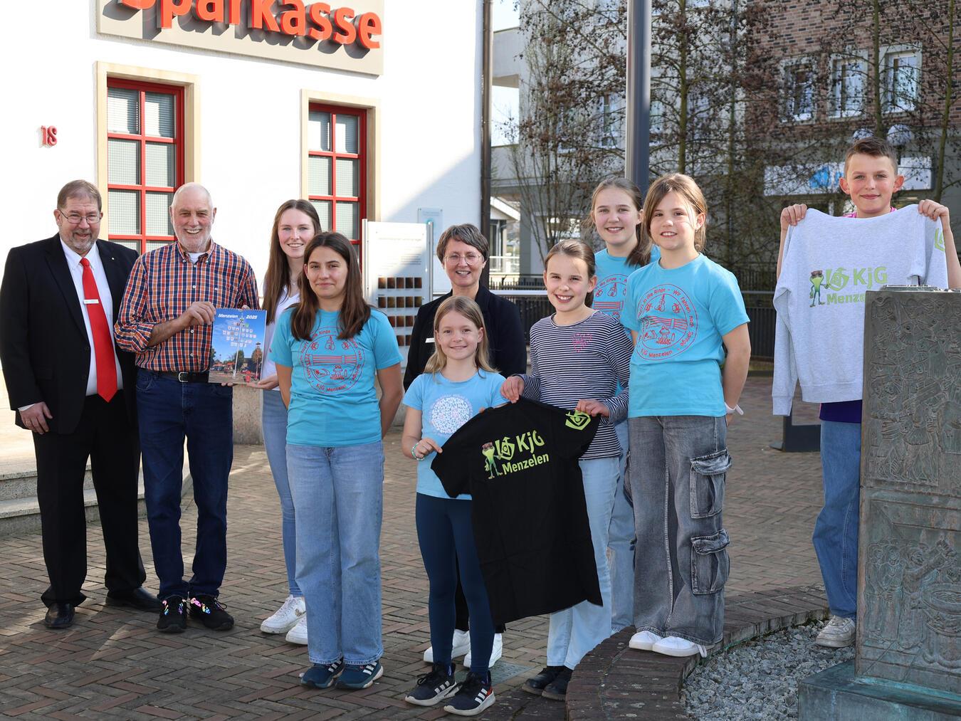 Kathrin Vingerhoet-Hoberg von der Pfarrleitung sowie Lia, Annalena, Laura, Maja, Tilda und Anton freuen sich aufs Sommerferienlager der KJG. Dafür spendete Hans-Josef Angenendt (2.v.l.) die mit dem Verkauf seiner Fotokalender erlösten 1.259,50 Euro. Die Sparkasse am Niederrhein gab weitere 250 Euro dazu und stockte damit die Spende auf insgesamt 1.509,50 Euro auf. Kundenberater Volger Oppers (l.) und die stellvertretende Geschäftsstellenleiterin Heike Letschert (6.v.l.) betonten, Hans-Josef Angenendts Engagement auch zukünftig unterstützen zu wollen. Foto: Sparkasse am Niederrhein