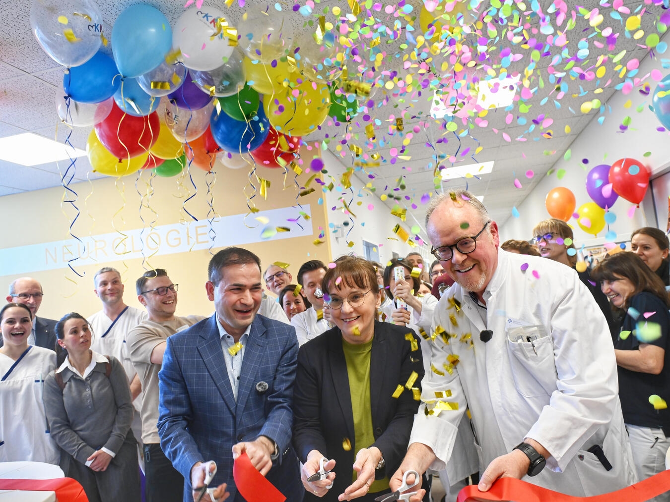 KKLE Geschäftsführer Sadık Taştan, KKLE-Geschäftsführerin Dr. Sabine Kisselbach, Chefarzt Dr. Christoph Baumsteiger (v.l.) beim Durchschneiden des traditionellen roten Bandes. Gleichzeitig zündet das Team der Neurologie den Konfettiregen. Foto: KKLE/Marc Albers