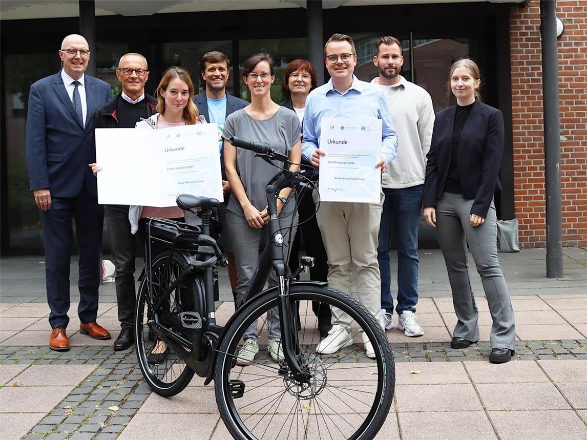 Landrat Christoph Gerwers (l.) und Brigitte Jansen (hinten, 3. v.r.), Geschäftsführerin der Wirtschaftsförderung Kreis Kleve, ehrten gemeinsam mit den Organisatoren des Kreises Kleve die erfolgreichsten Teilnehmenden der Aktion Stadtradeln: Melanie Fonk (vorne, l.) nahm den Preis als beste Einzel-Starterin entgegen. Für das Team der Kreisverwaltung erhielt stellvertretend Teamkapitän Alexander Beltermann (vorne, r.). die Urkunde. Foto: Kreis Kleve