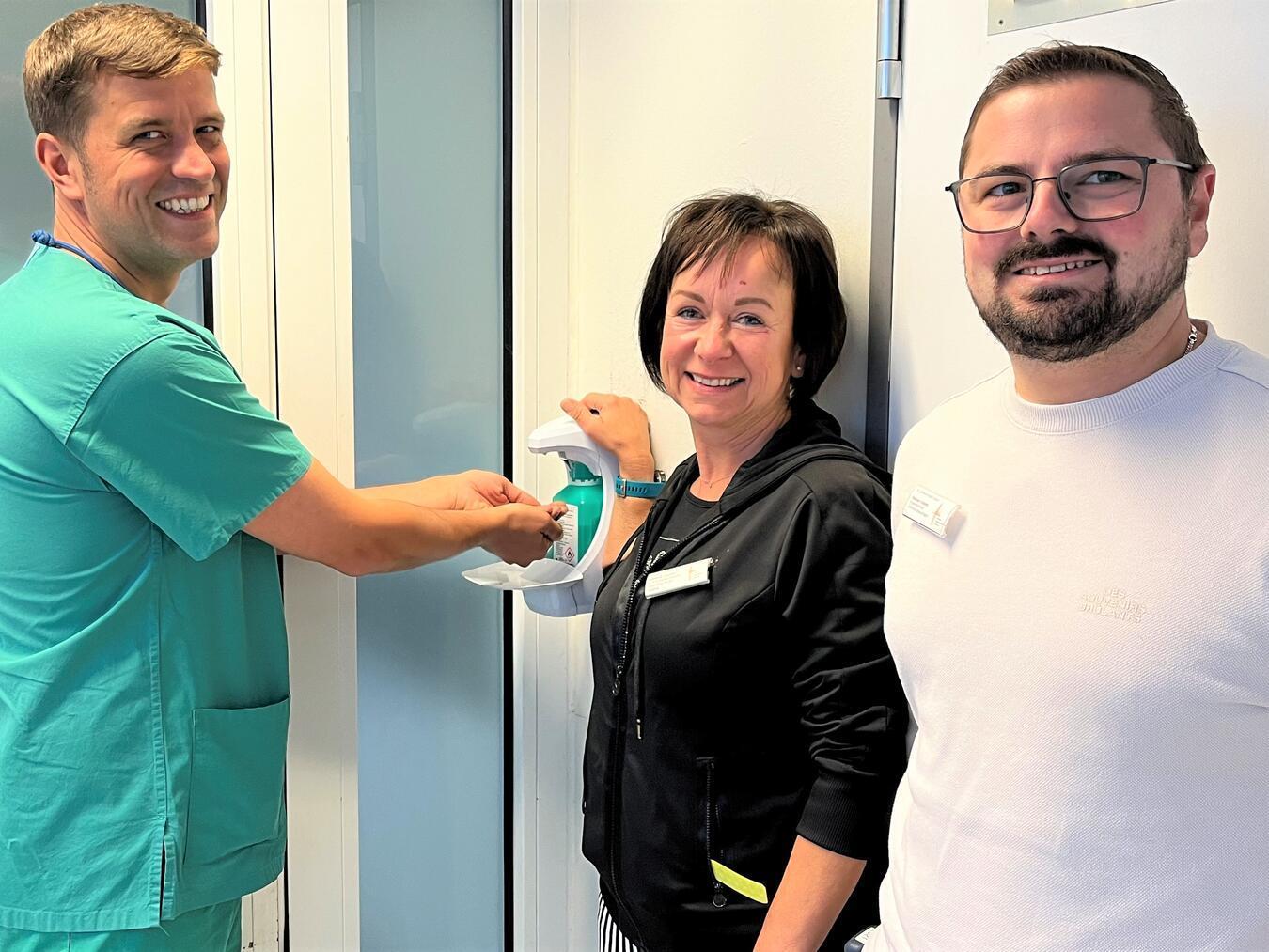 Lasse Engfeld (li.), Fachgesundheits- und Krankenpfleger für Intensivmedizin und Anästhesie, Isabella Zarden und Stefan Kösters, Hygienebeauftragte des St.-Clemens-Hospitals Geldern, freuen sich über die neuen Desinfektionsspender. Foto: St.-Clemens-Hospital