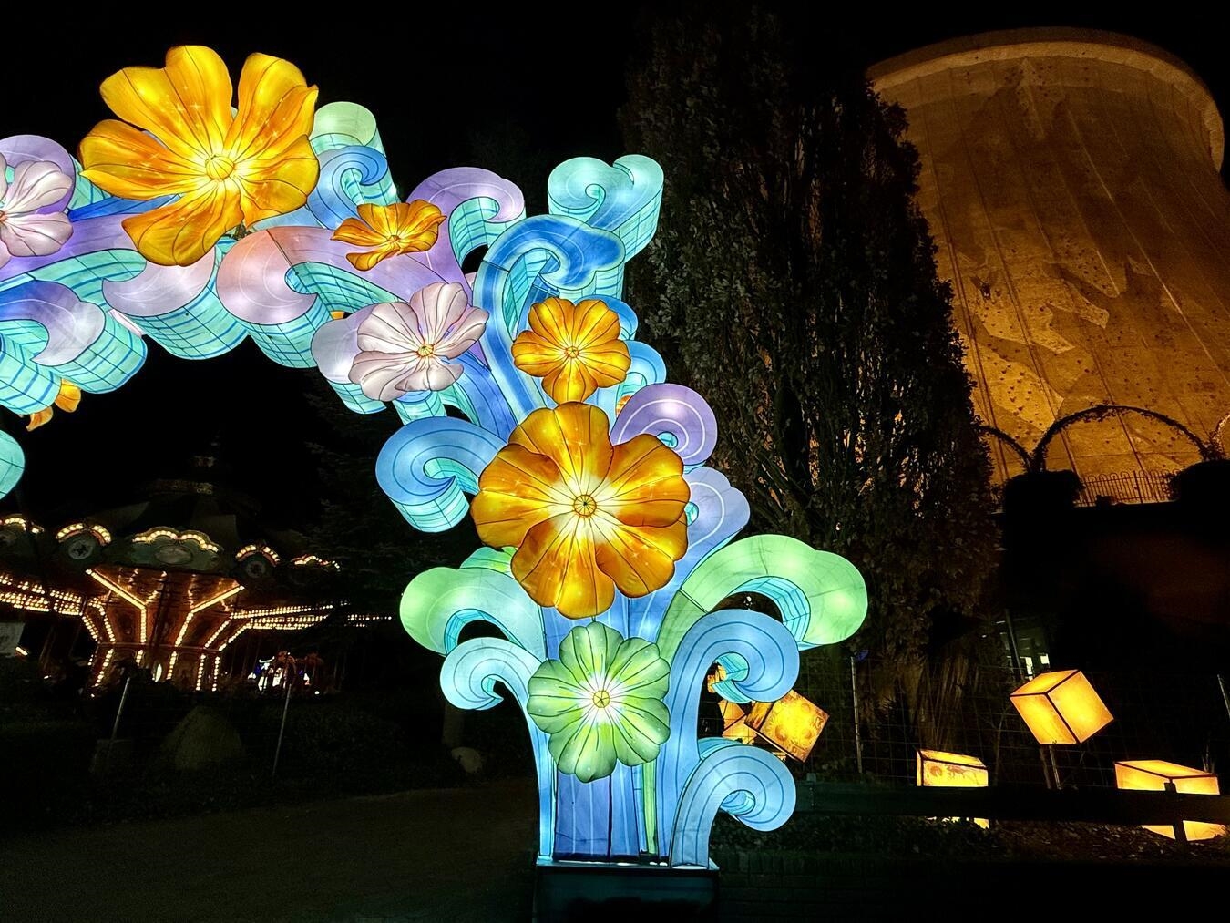 Leuchtende Blumen weisen den Weg – im Hintergrund ragt der beleuchtete Kühlturm des Wunderlands Kalkar in den Abendhimmel. NN-Foto: SP