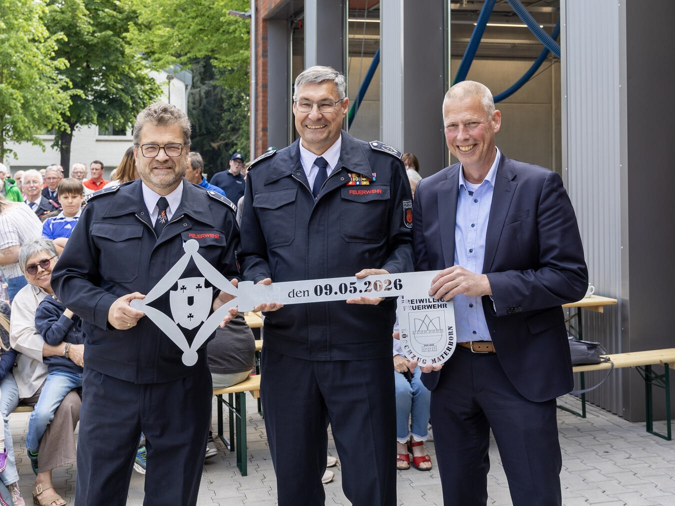 "Löschzugführer Ernst Vehreschild, Feuerwehrleiter Ralf Benkel und Bürgermeister Markus Dahmen bei Schlüsselübergabe vor Feuerwehrhaus"