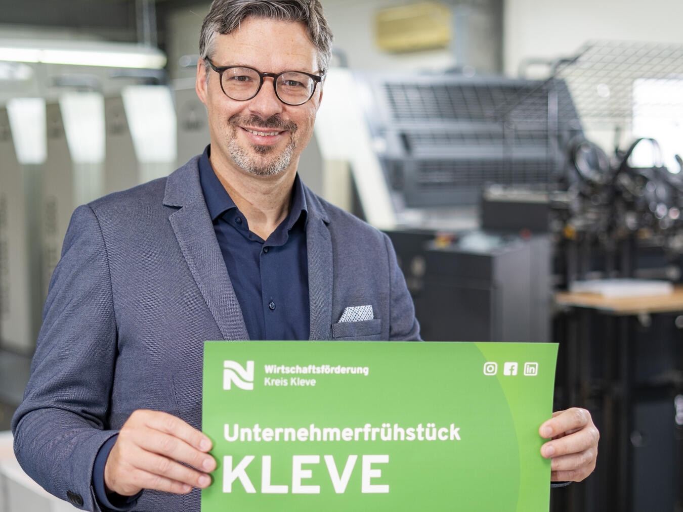 Marc Cattelaens von der Wirtschaftsförderung Kreis Kleve präsentiert das Plakat mit der Einladung zum Unternehmerfrühstück in Kleve. Foto: WFG/Gerhard Seybert