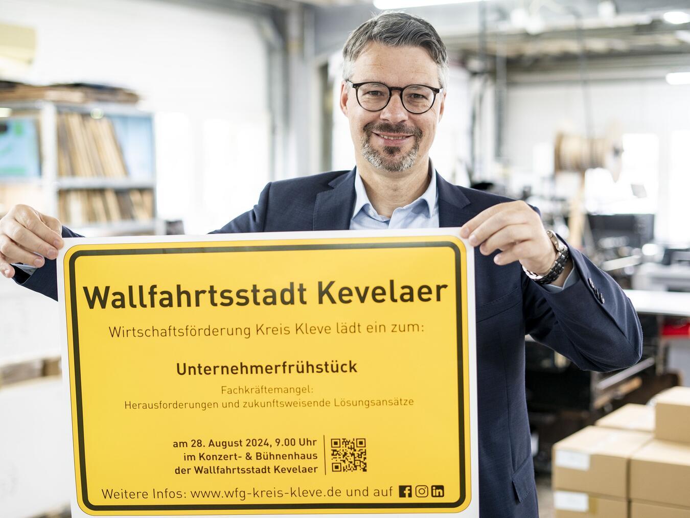 Marc Cattelaens von der Wirtschaftsförderung Kreis Kleve präsentiert das Ortsschild der Wallfahrtsstadt Kevelaer mit der Einladung zum Unternehmerfrühstück. Foto: Gerhard Seybert