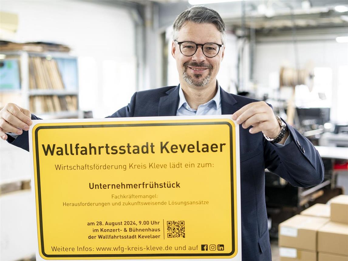Marc Cattelaens von der Wirtschaftsförderung Kreis Kleve präsentiert das Ortsschild der Wallfahrtsstadt Kevelaer mit der Einladung zum Unternehmerfrühstück. Foto: Gerhard Seybert