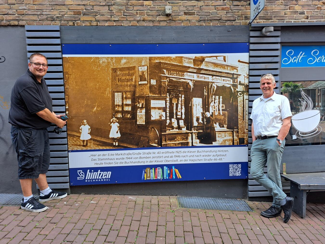 Matthias Hintzen (r.) als Ideengeber und Tim Tripp als Graphiker und Monteur vor dem historischen Foto der Buchhandlung Hintzen an der Marktstraße. Foto: privat