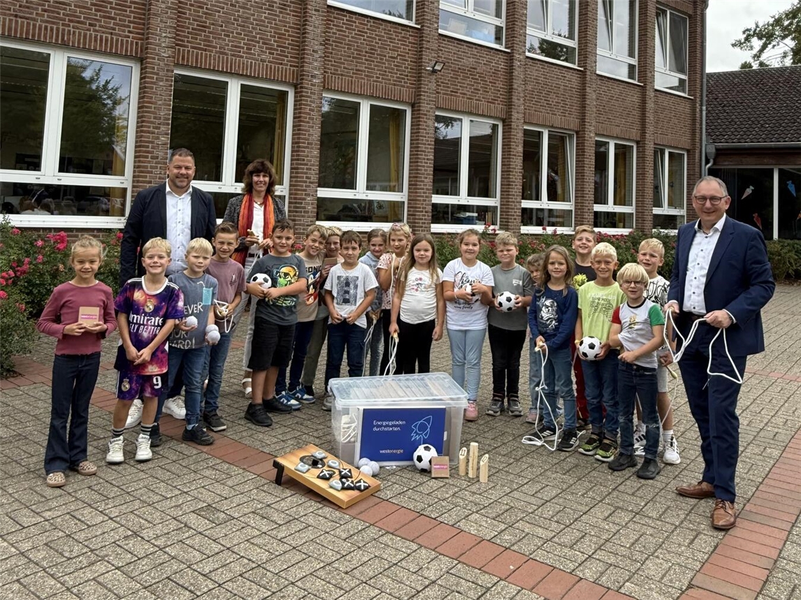 Mit Freude und Bewegung in den Schultag: Westenergie-Kommunalmanager Nils Rudolph übergibt der Schulleiterin Alexandra Peters ein Bewegungspaket. Bürgermeister Sebastian Hense freut sich über die neuen Möglichkeiten für aktive Pausen. Foto: Westenergie