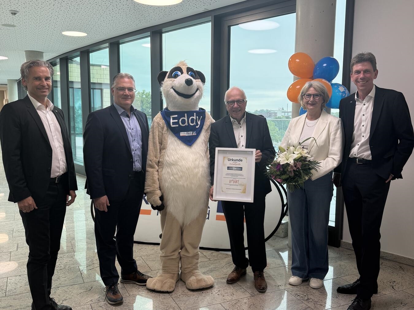 Nach fast zehn Jahren wurde jetzt in kleiner Runde der langjährige Markenbotschafter der Bank, Theo Brauer, verabschiedet. Auf dem Foto (v.l.): Christoph Thyssen (Prokurist), Severin-Peter Seidel (Vorstandsmitglied), Maskottchen Eddy, Theo Brauer, Jutta Brauer und Frank Ripkens (Vorstandsmitglied). Foto: Volksbank Kleverland