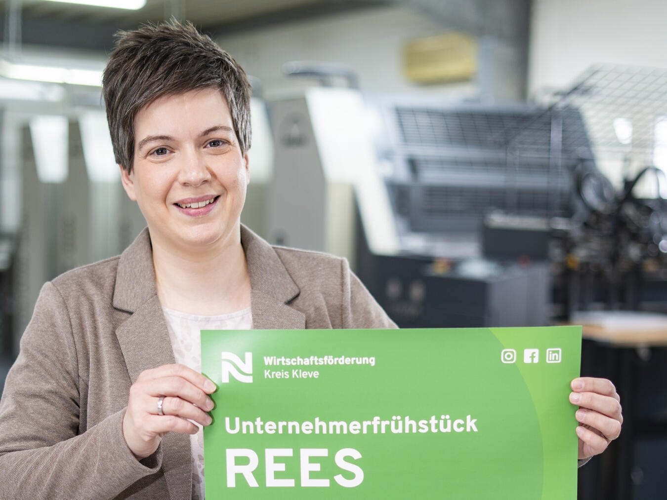 Nathalie Tekath-Kochs, Prokuristin der Wirtschaftsförderung Kreis Kleve, präsentiert das Plakat mit der Einladung zum Unternehmerfrühstück in Rees. Foto: Gerhard Seybert