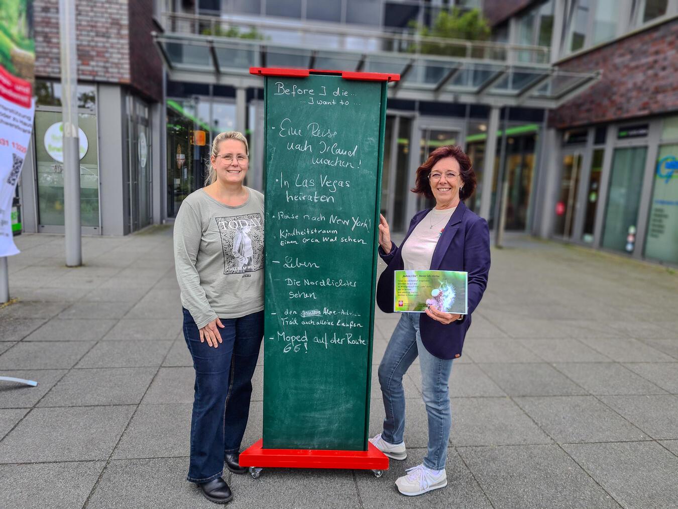 Nicole Schoeters und Franziska Eickmans vom ambulanten Hospizdienst vor der Kreidewand „Before I die...“.Foto: Caritasverband Geldern-Kevelaer