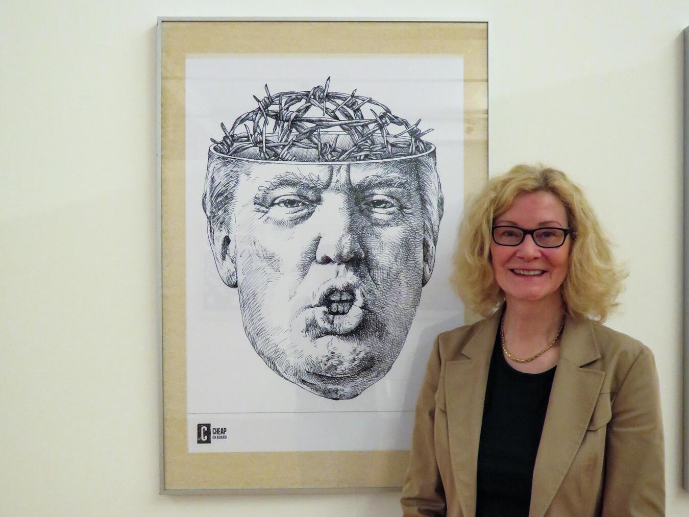 PAN-Kuratorin Christiane van Haaren mit einem Plakat zum einem Thema, mit dem sich Tomaso Marcolla intensiver beschäftigt: US-Präsident Donald Trump und dessen Grenzpolitik. NN-Foto: Gerhard Seybert