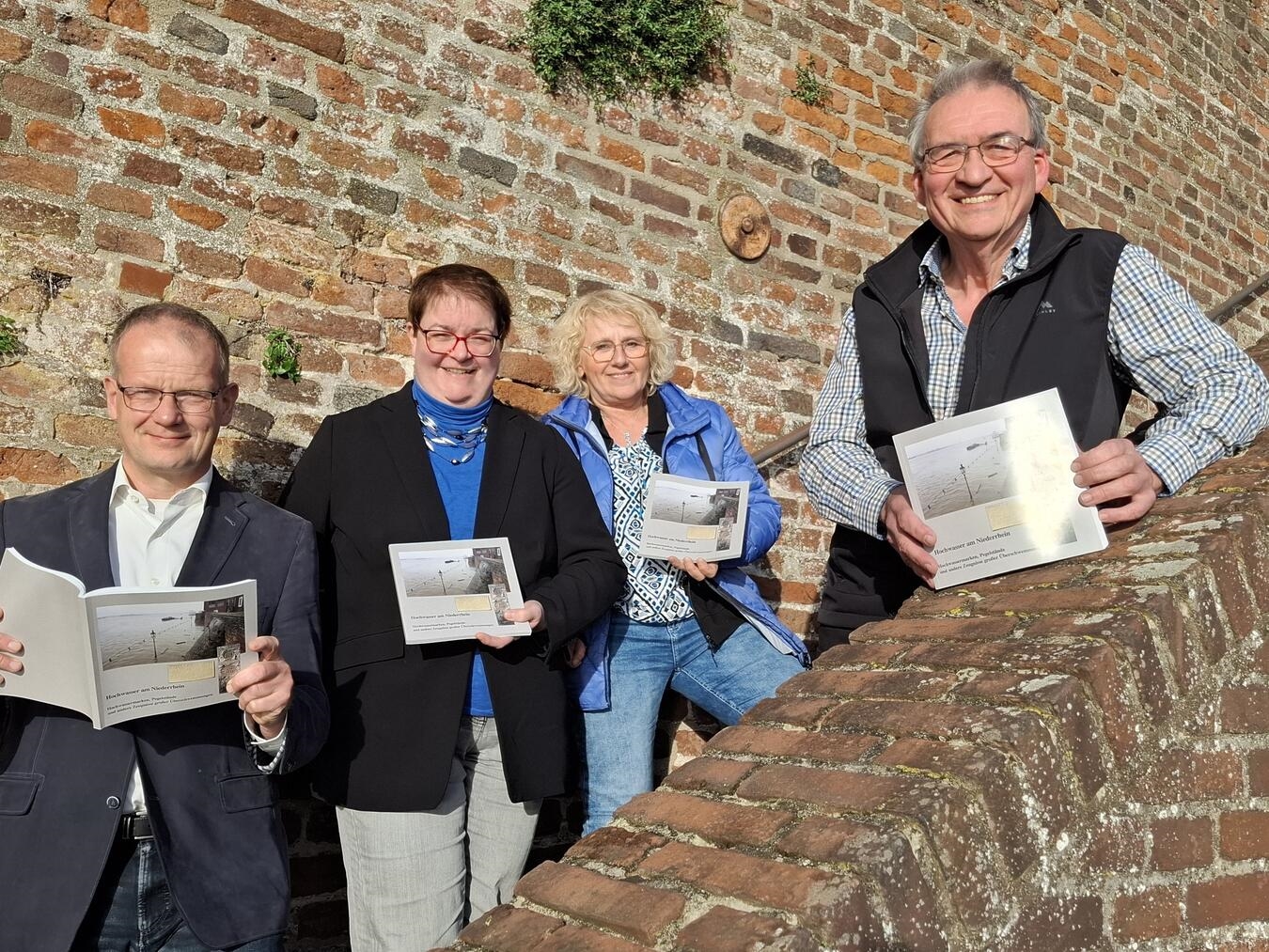 Peter von Bein (r.) stellt sein neues Buch im Beisein von Büchereileiter Thomas Dierkes, Fachbereichsleiterin Sigrid Mölleken und Stadtarchivarin Tina Oostendorp (v. li.) vor. Im Hintergrund ist eine Hochwassermarke von 1883 zu sehen. Foto: Stadt Rees