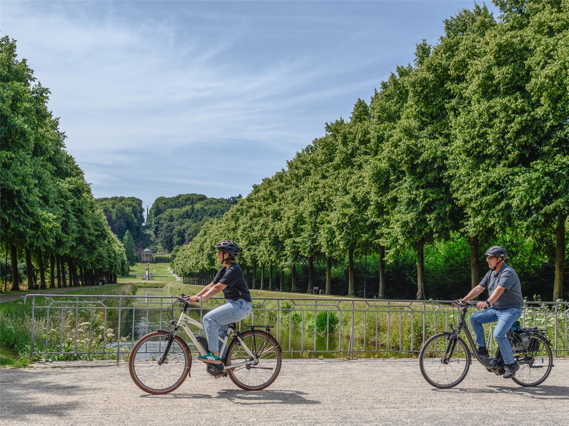 "Radfahrer fährt durch grüne Gartenanlagen bei Sonnenschein, Erholung in der Natur"