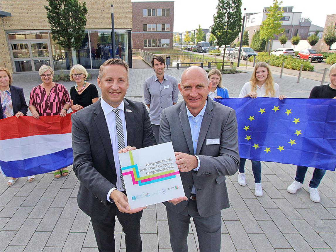Regierungspräsident Thomas Schürmann (vorne li.) überreicht Schulleiter Andreas Boland (re.) die Auszeichnung. Mit ihnen freuen sich (hintere Reihe v. l.) die allgemeine Vertreterin des Landrates Kreis Kleve, Zandra Boxnick, Gelderns stellvertretende Bürgermeisterin Bärbel Wolters, die Schulfachliche Dezernentin bei der Bezirksregierung, Alexandra Donike, Stephan Schmitz (Euregio-Beauftragter Berufskolleg Geldern), Rahel Beus (Auszubildende Kreispolizeibehörde Kleve), Fabienne Verdijk (Auszubildende bei der Kreisverwaltung Kleve) und Lois de Winkel (Auszubildender im Gartenbaubetrieb Christian Heufs).NN-Foto: Theo Leie