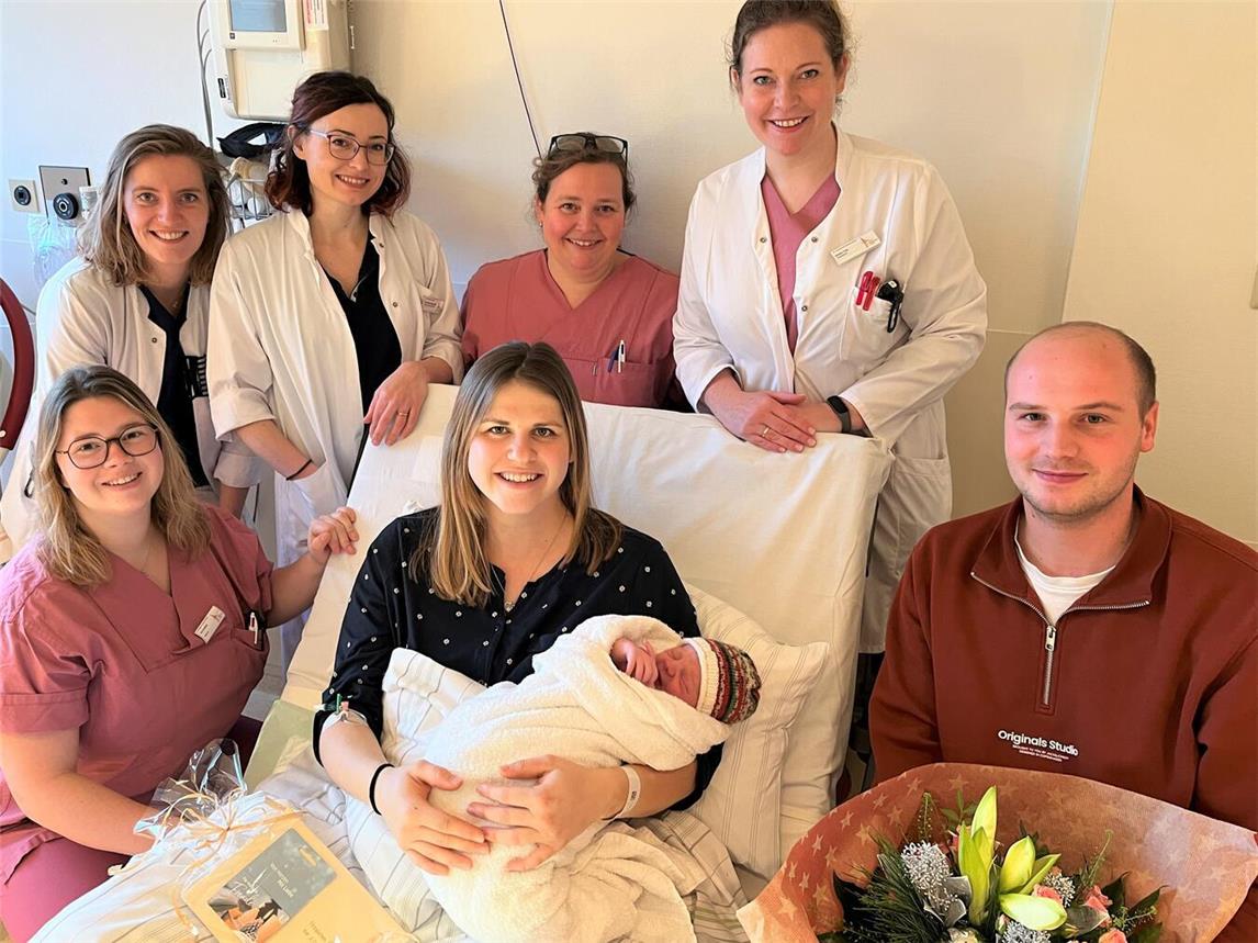 Saskia und Dominik Stülpner mit Sohn Johann (vorne) aus Kamp-Lintfort wurden von den Oberärztinnen Evelyn Frey und Donalda Surducki sowie Assistenzärztin Bente Pruijssers (hintere Reihe von links nach rechts im weißen Kittel) und den beiden Hebammen Katharina Leenen (hinten) und Pia Gutsfeld (links) mit einem Blumenstrauß und einem Geschenkgutschein zur 1.000. Geburt in 2024 im St.-Clemens-Hospital beglückwünscht. Foto: Elke Wiegmann/St.-Clemens-Hospital