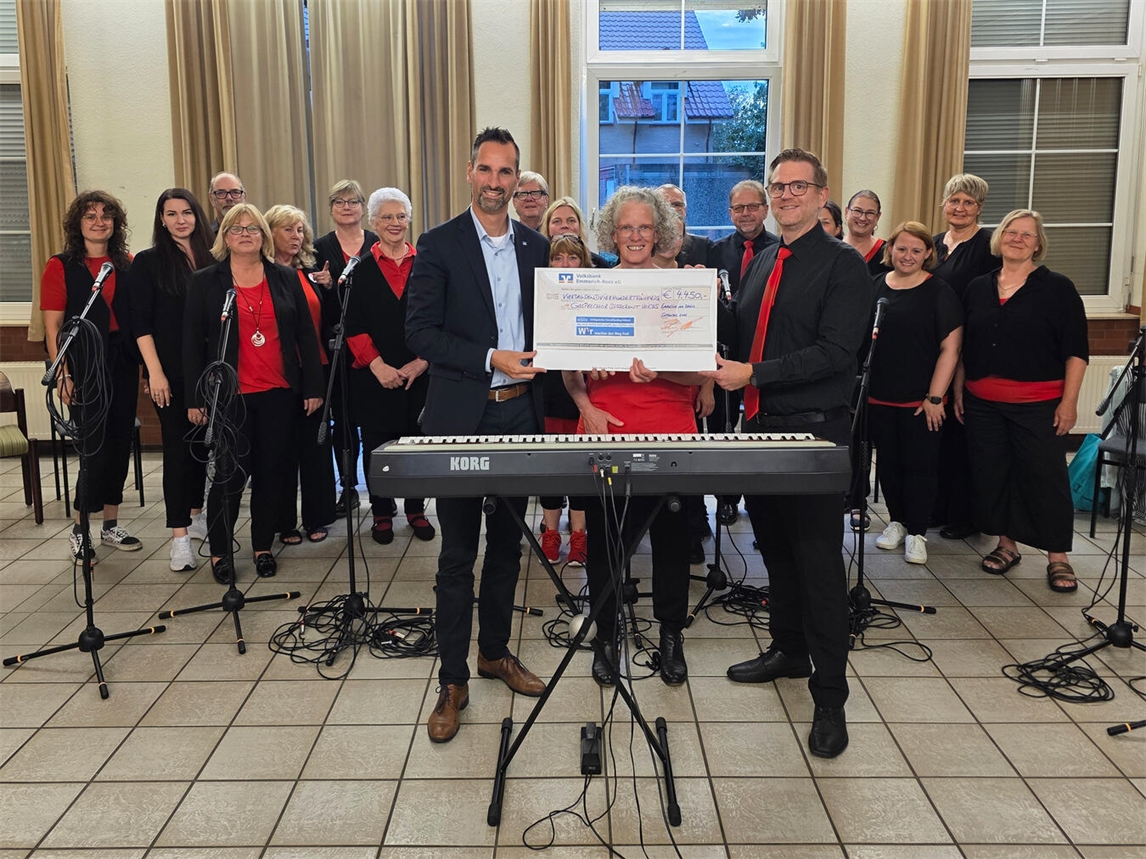 "Scheckübergabe beim Chor Different Voices, Chormitglieder lächeln, Unterstützung für Musikprojekte"