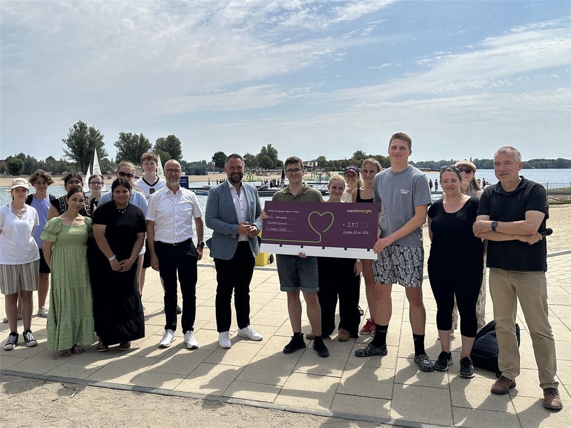 Schülerinnen und Schüler der Willi-Fährmann-Gesamtschule erhalten im Rahmen einer Scheckübergabe das Preisgeld für ihre Teilnahme am Westenergie Distanz Duell. Foto: Westenergie AG