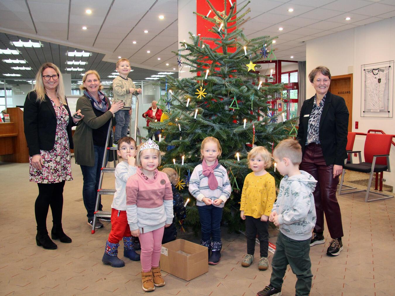 Sechs Kinder der evangelischen Kita schmückten den Tannenbaum in der Alpener Sparkasse. Kathrin Hüsch (v.l.n.r.), Myriam Pockrandt und Heike Letschert halfen mit. Foto: Sparkasse