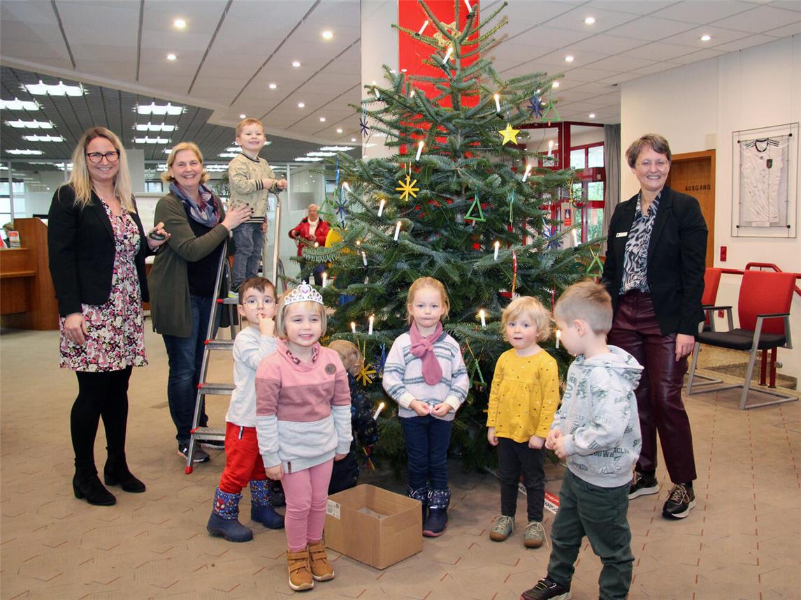 Sechs Kinder der evangelischen Kita schmückten den Tannenbaum in der Alpener Sparkasse. Kathrin Hüsch (v.l.n.r.), Myriam Pockrandt und Heike Letschert halfen mit. Foto: Sparkasse