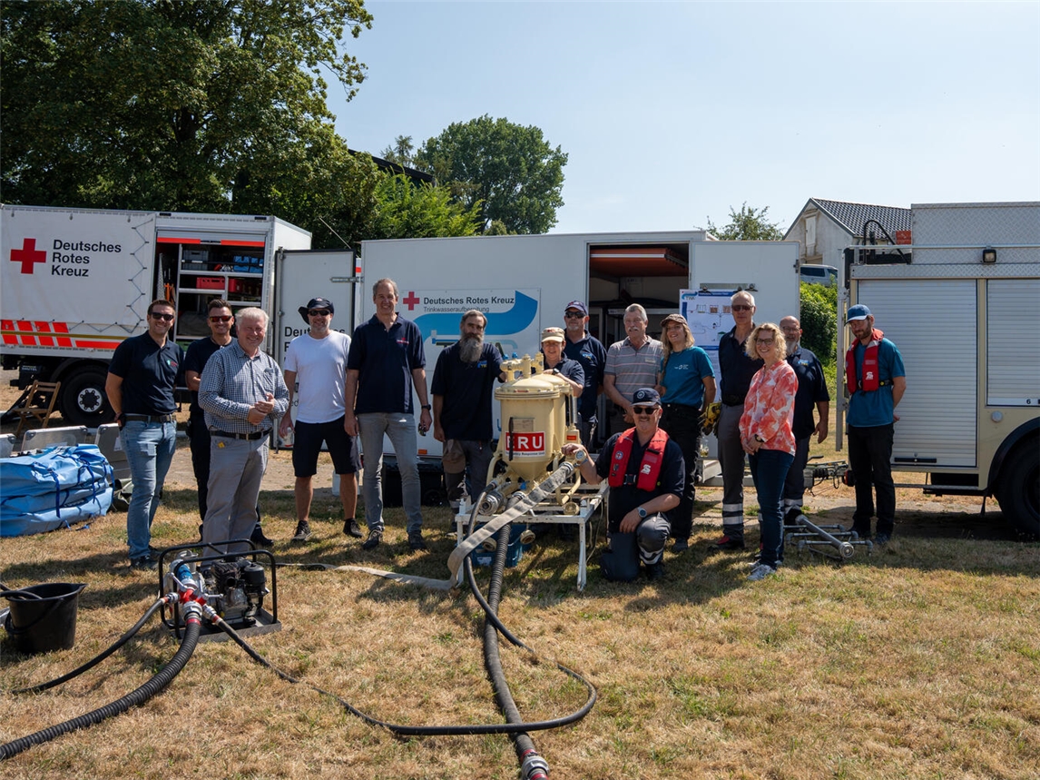 Vertreterinnen und Vertreter des Kreises Wesel informierten sich beim DRK-Kreisverband Niederrhein über die Möglichkeiten der mobilen Trinkwasseraufbereitung im Bevölkerungsschutz. Mit dabei waren Janina Schmidt-Jakisch (Gesundheitsamt Kreis Wesel), Frank Brändel (Leiter Fachdienst Sicherheit und Ordnung), Sven Rissel (Krisenmanagement) sowie Niklas Killewald (Leiter der Kreisleitstelle Wesel). Ebenfalls auf dem Bild sind Vertreter des Präsidiums des DRK Kreisverbandes Niederrhein sowie Mitglieder der Fachgruppe Technik & Sicherheit und der TWA-Gruppe (Trinkwasseraufbereitung) zu sehen. Foto: Silas Thekook/DRK