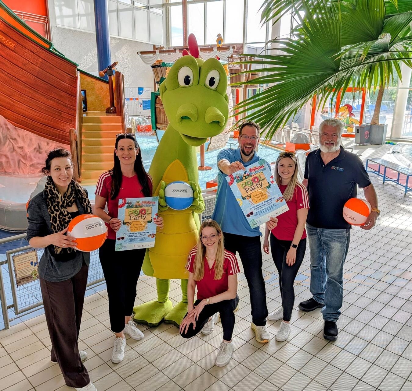 Gruppe junger Freunde lächelt vor einem Schwimmbad für eine Poolparty, Sommerfreude, Stadtwerke Goch Bäder GmbH.