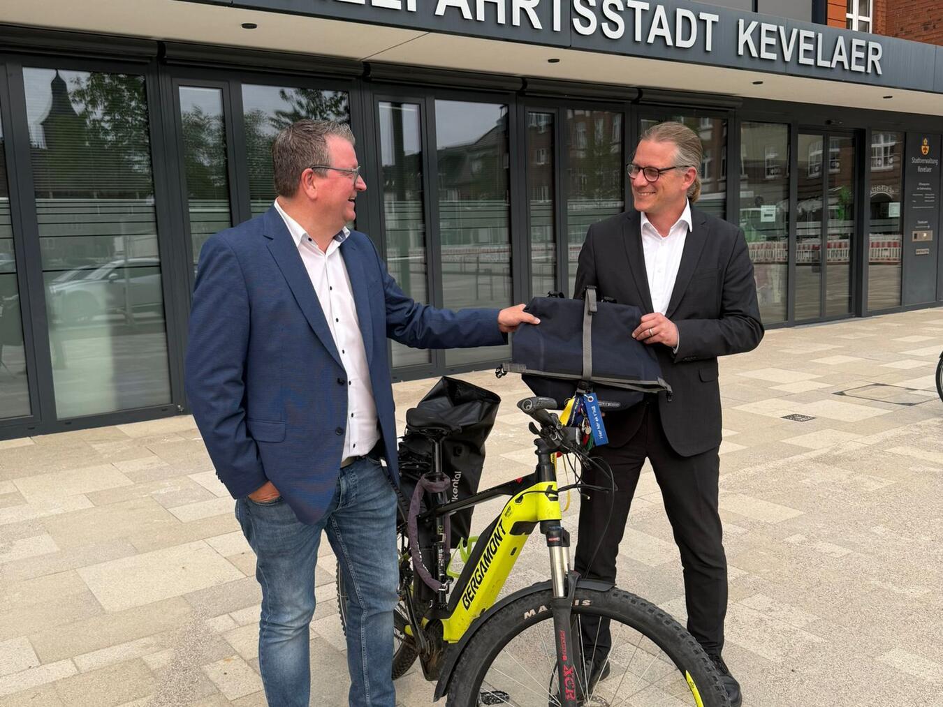 Weezes Bürgermeister Georg Koenen hat die Fahrradtasche an Kevelaers Bürgermeister Dr. Dominik Pichler überreicht. Foto: Gemeinde Weeze