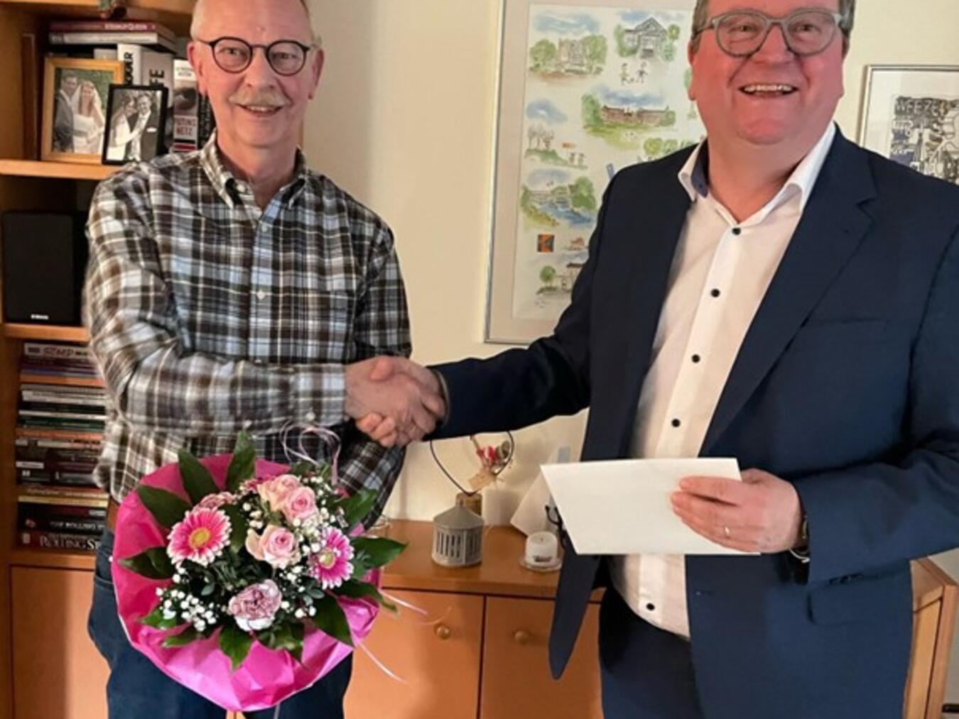 Weezes Bürgermeister Georg Koenen (r. )bedankt sich bei Johannes van Hall mit einem Blumenstrauß und einem Gutschein für seine 30jährige Tätigkeit in der Macherey-Stiftung. Foto: privat