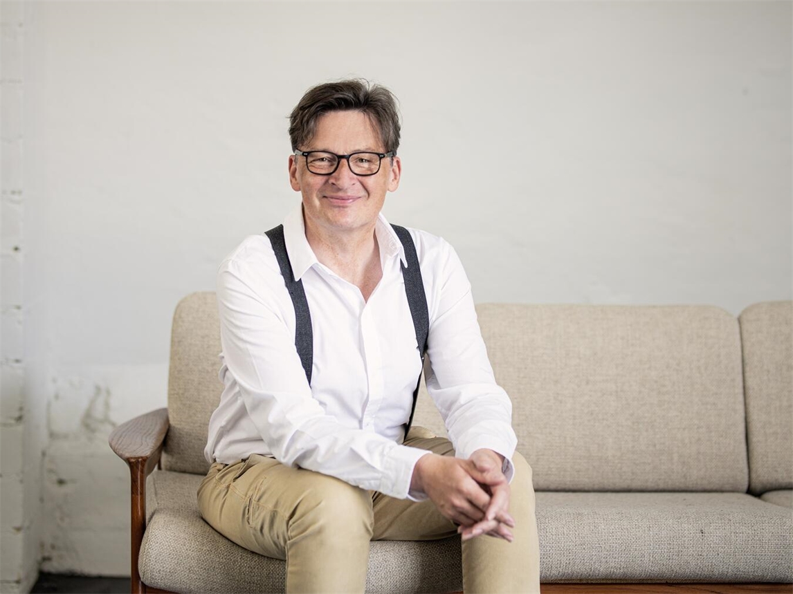 Kabarettist Stefan Verhasselt auf Bühne mit Programm „6.0“, lachende Zuschauer im Hintergrund. Foto von Simon Erath.