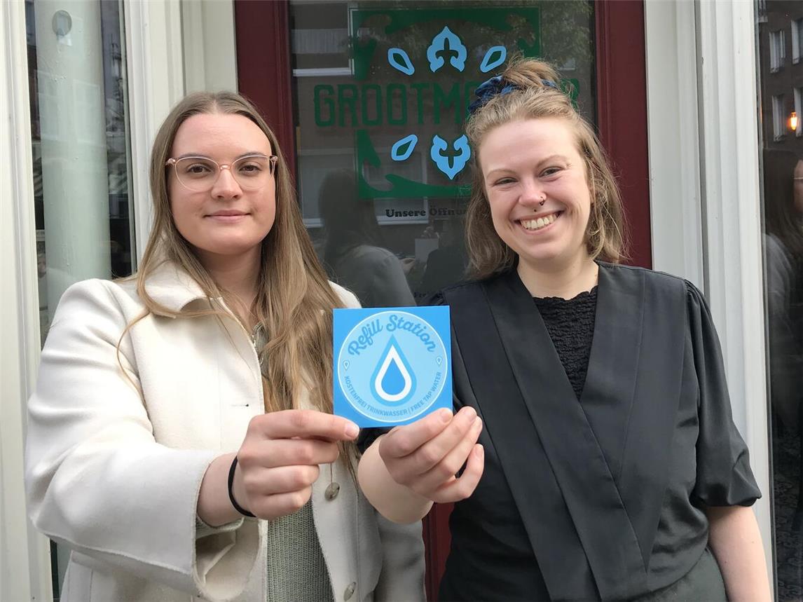 Werben für die neue Initiative: Emmerichs Klimaschutzmanagerin Celine Breuer (l.) und Sophie-Zoe Kroh vom Café Grootmoeder präsentieren das Logo von Refill Deutschland. Foto: Stadt Emmerich
