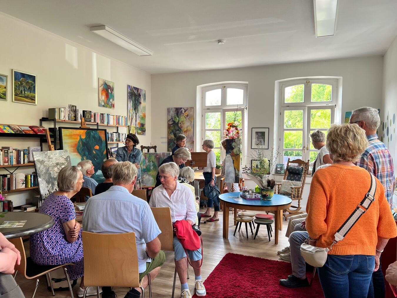 "Kunstfreunde bei Ausstellungseröffnung in Bücherei Bienen, lebhafte Besuchergruppe vor Kunstwerken"